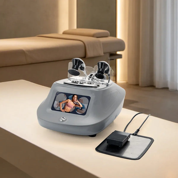 A tecar therapy beauty device with dual black applicator heads sits on a beige table in a spa-like room, with a black charging pad and cable beside it and a massage table in the background.