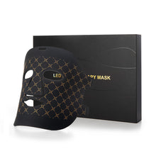 Black LED facial mask with a gold geometric pattern, shown next to its black packaging box on a white background.